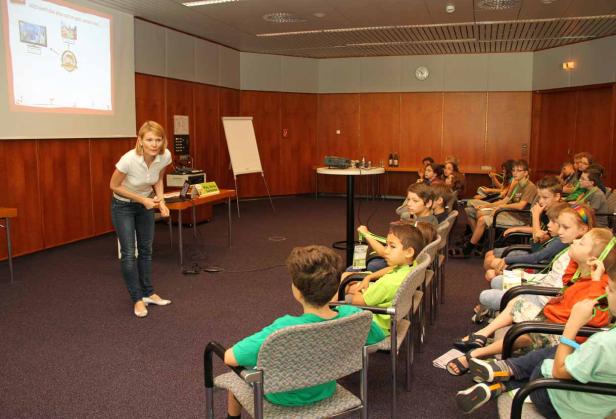 Eine Frau hält einen Vortrag vor einer Gruppe von Kindern in einem Konferenzraum.