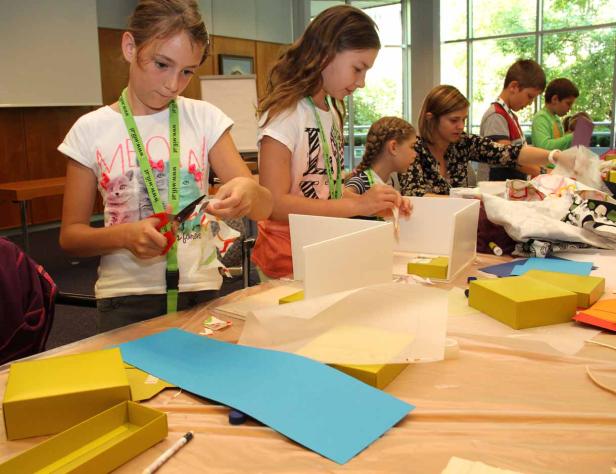 Kinder basteln an einem Tisch mit Scheren, Papier und Kartons.