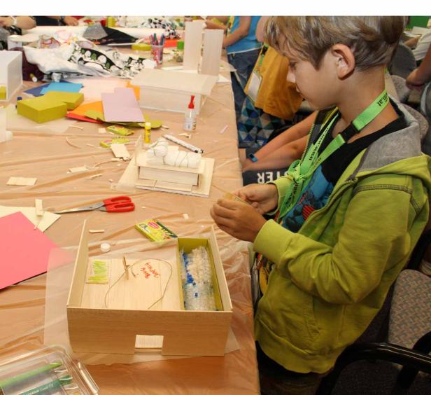 Ein Junge bastelt an einem Holzkasten auf einem Tisch voller Bastelmaterialien.
