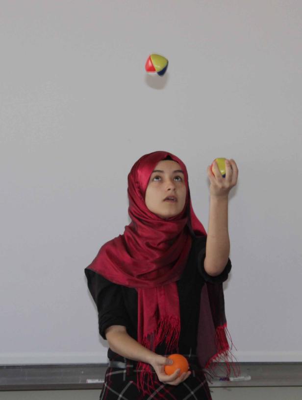 Eine junge Frau mit Hijab jongliert mit drei Bällen.