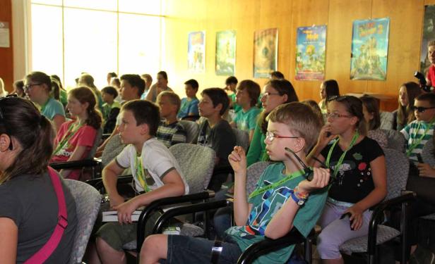 Eine Gruppe von Kindern sitzt in einem Raum und schaut aufmerksam zu.