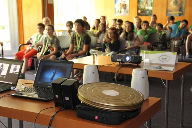 Eine Gruppe von Kindern schaut in einem Raum einen Film mit einem Projektor.