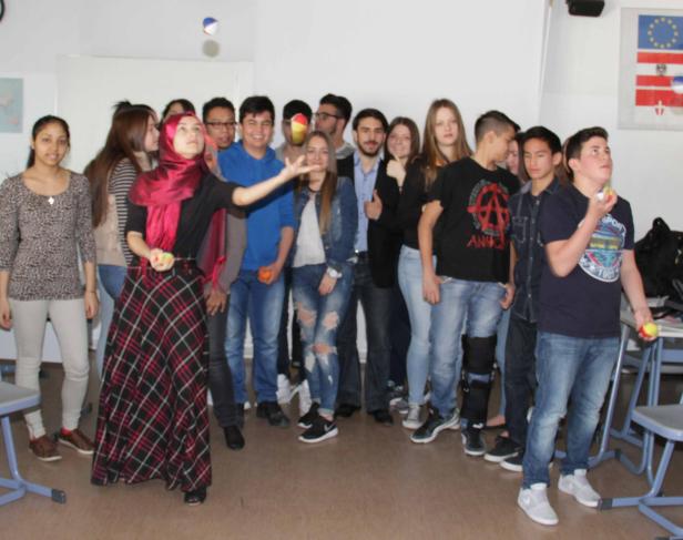 Eine Gruppe von Studenten steht in einem Klassenzimmer, eine Frau jongliert mit Bällen.