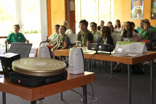 Eine Gruppe von Kindern schaut in einem Raum einen Film, projiziert von einem Projektor.