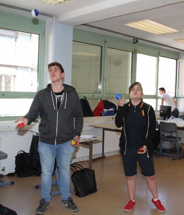 Zwei Personen jonglieren mit Bällen in einem Klassenzimmer.