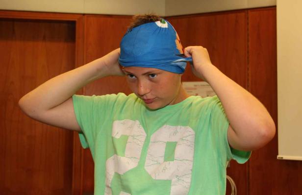 Ein Jugendlicher bindet sich ein blaues Tuch um den Kopf.