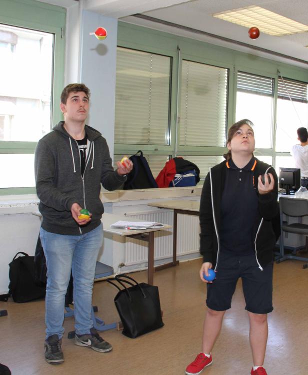 Zwei Jugendliche jonglieren mit bunten Bällen in einem Klassenzimmer.