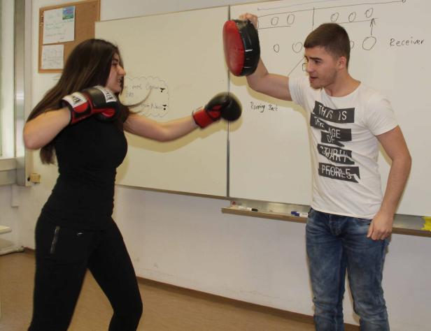 Eine junge Frau boxt mit einem Trainer in einem Klassenzimmer.