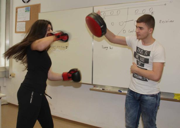 Eine junge Frau boxt mit einem Trainer vor einer Tafel.