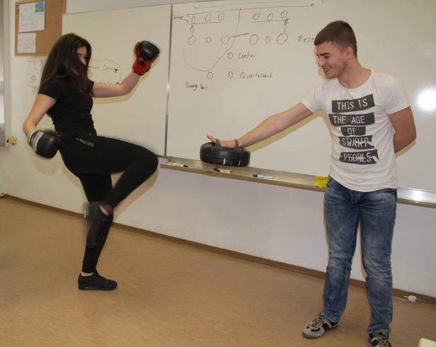 Eine Frau mit Boxhandschuhen führt einen Tritt gegen ein Schlagkissen, das von einem Mann gehalten wird.