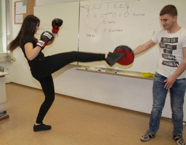 Eine Frau mit Boxhandschuhen führt einen Tritt gegen ein Schlagpolster aus, das ein Mann hält.