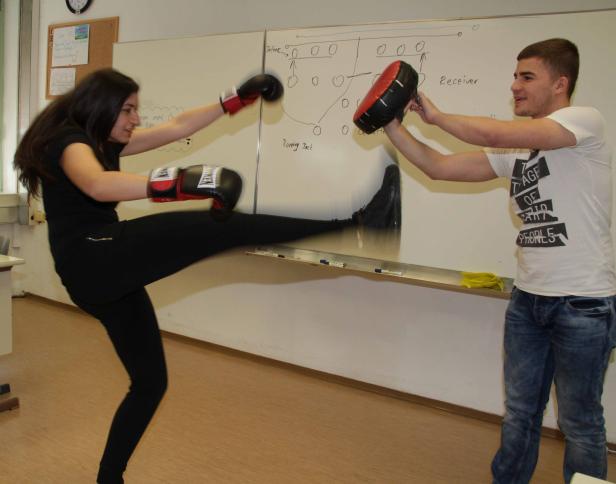 Eine Frau mit Boxhandschuhen führt einen Tritt gegen ein Schlagpolster, das von einem Mann gehalten wird.