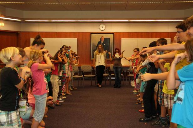 Eine Gruppe Kinder ahmt mit zwei Betreuern eine Bewegung nach.