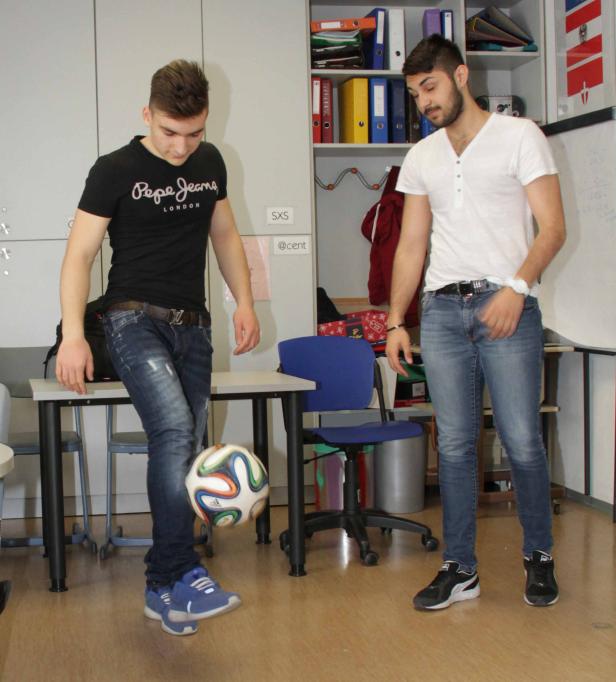 Zwei junge Männer spielen in einem Raum mit einem Fußball.