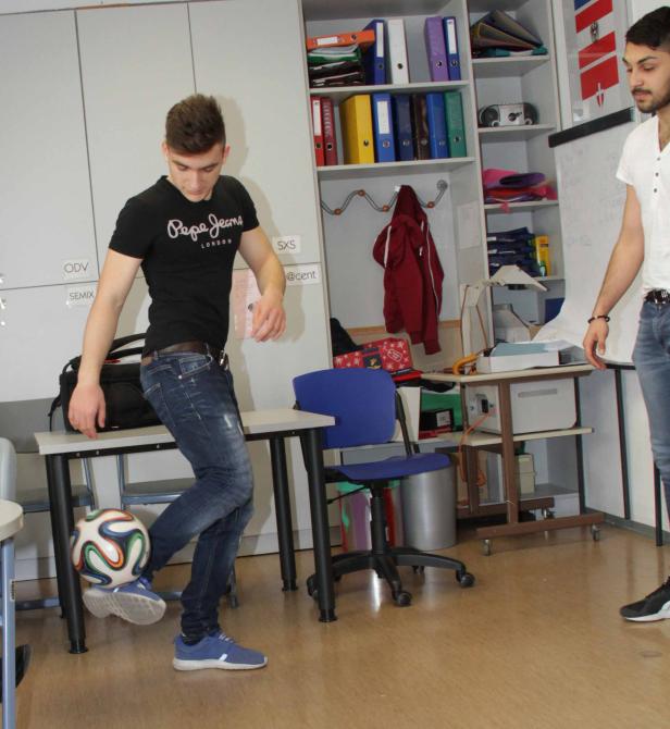 Ein junger Mann balanciert einen Fußball auf seinem Fuß in einem Klassenzimmer.