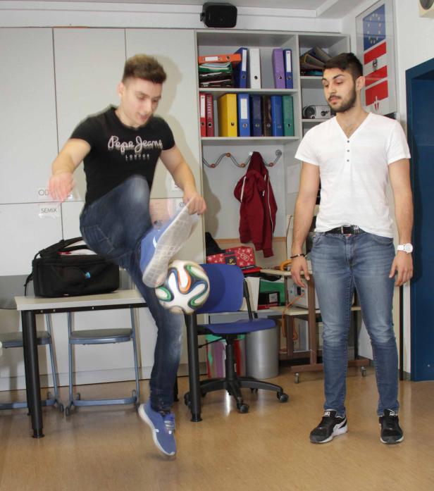 Ein junger Mann jongliert mit einem Fußball, während ein anderer zusieht.