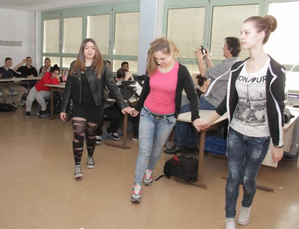 Drei junge Frauen halten Händchen und gehen durch ein Klassenzimmer.