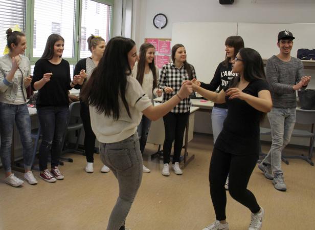 Eine Gruppe junger Leute tanzt und klatscht in einem hellen Raum.