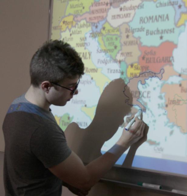 Ein Mann umreißt mit einem Stift Griechenland auf einer Europakarte.