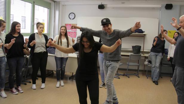 Eine Gruppe von Menschen tanzt im Kreis in einem Klassenzimmer.
