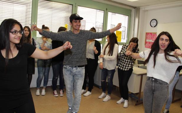 Eine Gruppe junger Leute tanzt in einem Klassenzimmer.