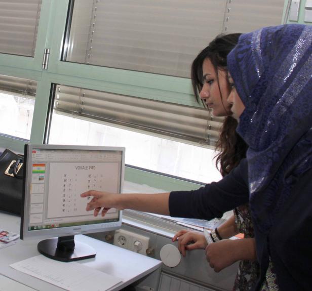 Zwei Frauen betrachten einen Computerbildschirm mit einer Tabelle von Vokalen in Hindi.