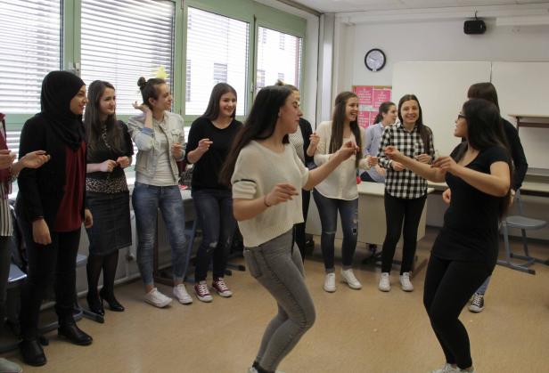 Eine Gruppe junger Frauen tanzt und lacht in einem hellen Raum.