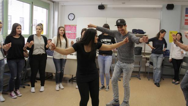 Eine Gruppe junger Leute tanzt im Kreis in einem Klassenzimmer.