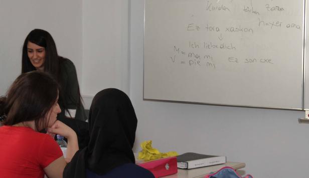 Drei Frauen sitzen in einem Klassenzimmer vor einer Tafel mit Notizen.