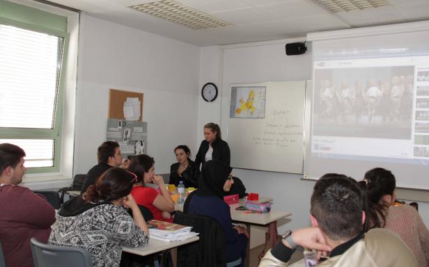Eine Lehrerin steht vor einer Klasse und erklärt etwas anhand einer Projektion und einer Tafel.