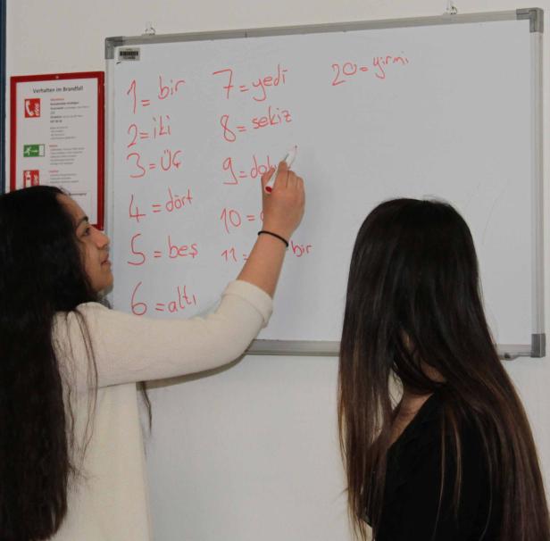 Eine Frau schreibt türkische Zahlen auf eine weiße Tafel.