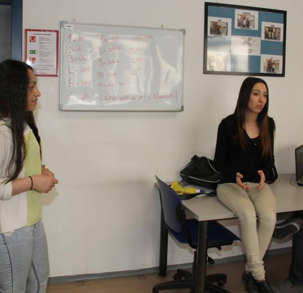 Zwei junge Frauen in einem Klassenzimmer mit einer Tafel, auf der Türkisch unterrichtet wird.