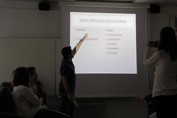 Ein Mann präsentiert eine Folie über Sprachen und Religionen vor einem Publikum.