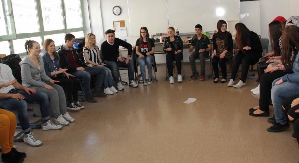 Eine Gruppe von Teenagern sitzt im Kreis und klatscht in die Hände.