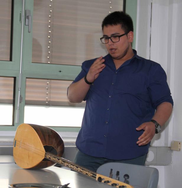 Ein Mann mit Brille gestikuliert neben einer Saz, einem traditionellen türkischen Saiteninstrument.