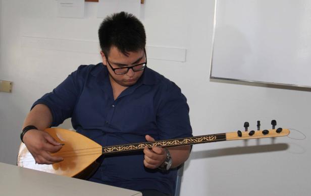 Ein Mann mit Brille spielt ein Saiteninstrument, möglicherweise eine Saz.