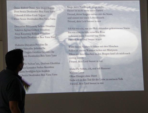Eine Person steht vor einer Projektion mit türkischen und deutschen Gedichten.