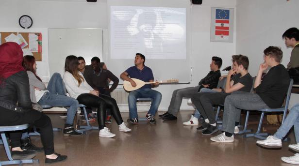 Eine Gruppe von Jugendlichen sitzt im Kreis, ein junger Mann spielt Saz und singt.