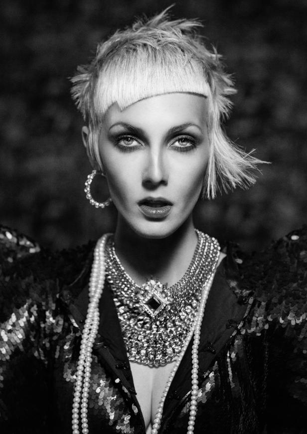 Schwarzweißporträt einer Frau mit auffälligem Schmuck und asymmetrischem Haarschnitt.