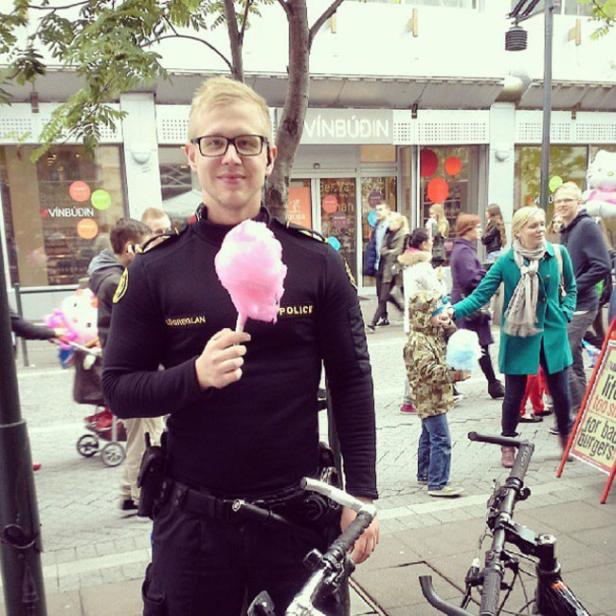 Ein Polizist in Uniform hält eine rosa Zuckerwatte in der Hand.