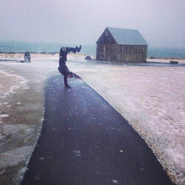 Eine Person macht einen Handstand auf einem vereisten Weg in Küstennähe.