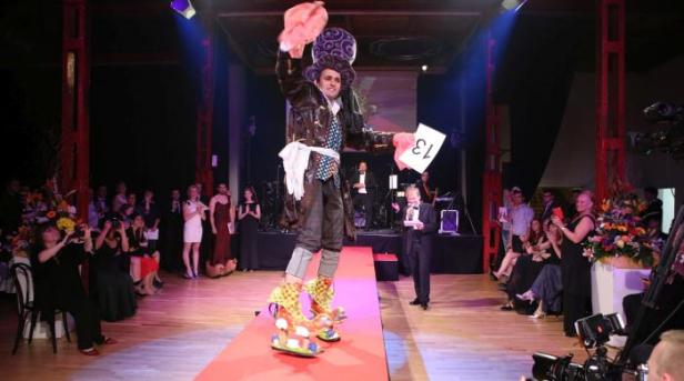 Ein Mann im Kostüm des verrückten Hutmachers läuft über einen roten Teppich vor Publikum.