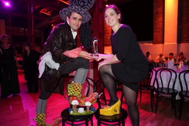 Ein Mann im Kostüm und eine Frau posieren mit ausgefallenen Schuhen und einer Trophäe.