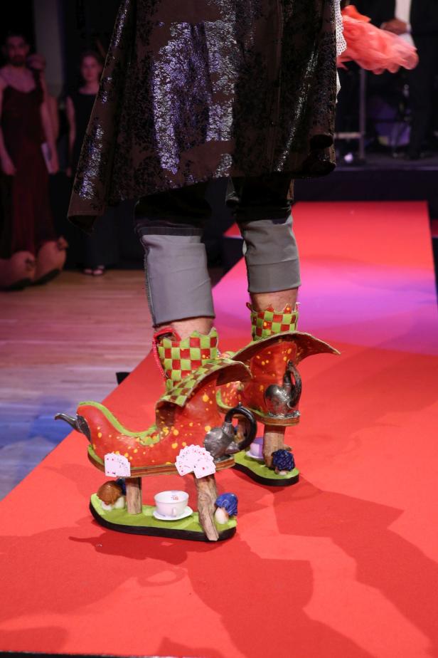 Ein Model präsentiert extravagante Schuhe in Form von Teekannen auf dem Laufsteg.