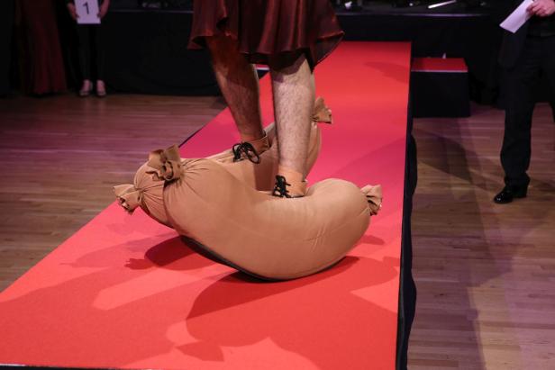 Eine Person trägt übergroße, wurstförmige Schuhe auf einem roten Teppich.