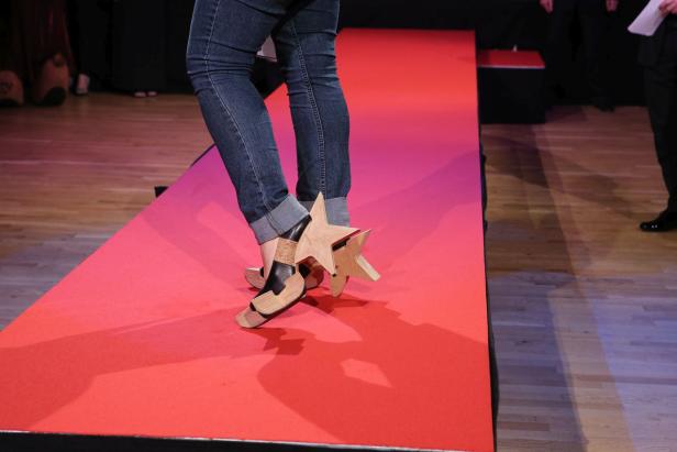 Eine Person mit Jeans und ungewöhnlichen Schuhen mit Holzsternen auf einem roten Teppich.