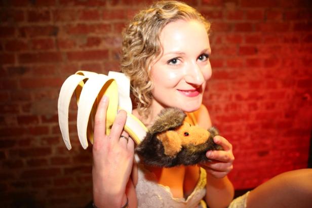 Eine Frau hält eine Bananentasche und ein Plüschtier vor einer roten Backsteinmauer.