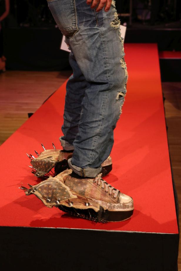 Ein Model präsentiert extravagante, mit Nieten besetzte Turnschuhe auf einem Laufsteg.