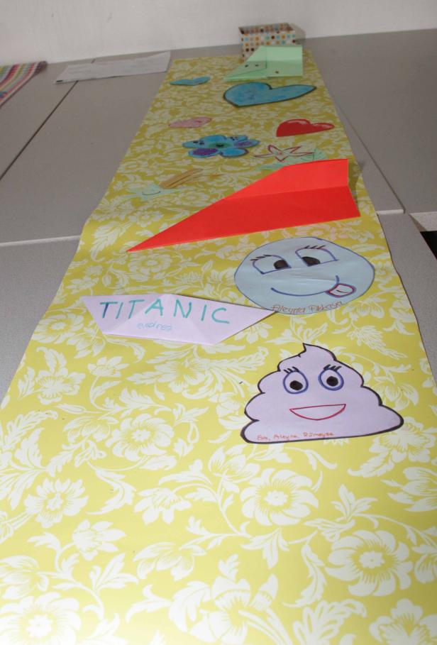 Eine gelbe Tischdecke mit verschiedenen Papierformen, darunter ein rotes Papierflugzeug und ein Papierboot mit der Aufschrift „Titanic“.