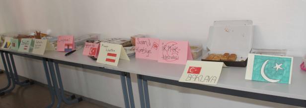 Auf einem Tisch stehen verschiedene Süßspeisen mit handgeschriebenen Schildern und Länderflaggen.